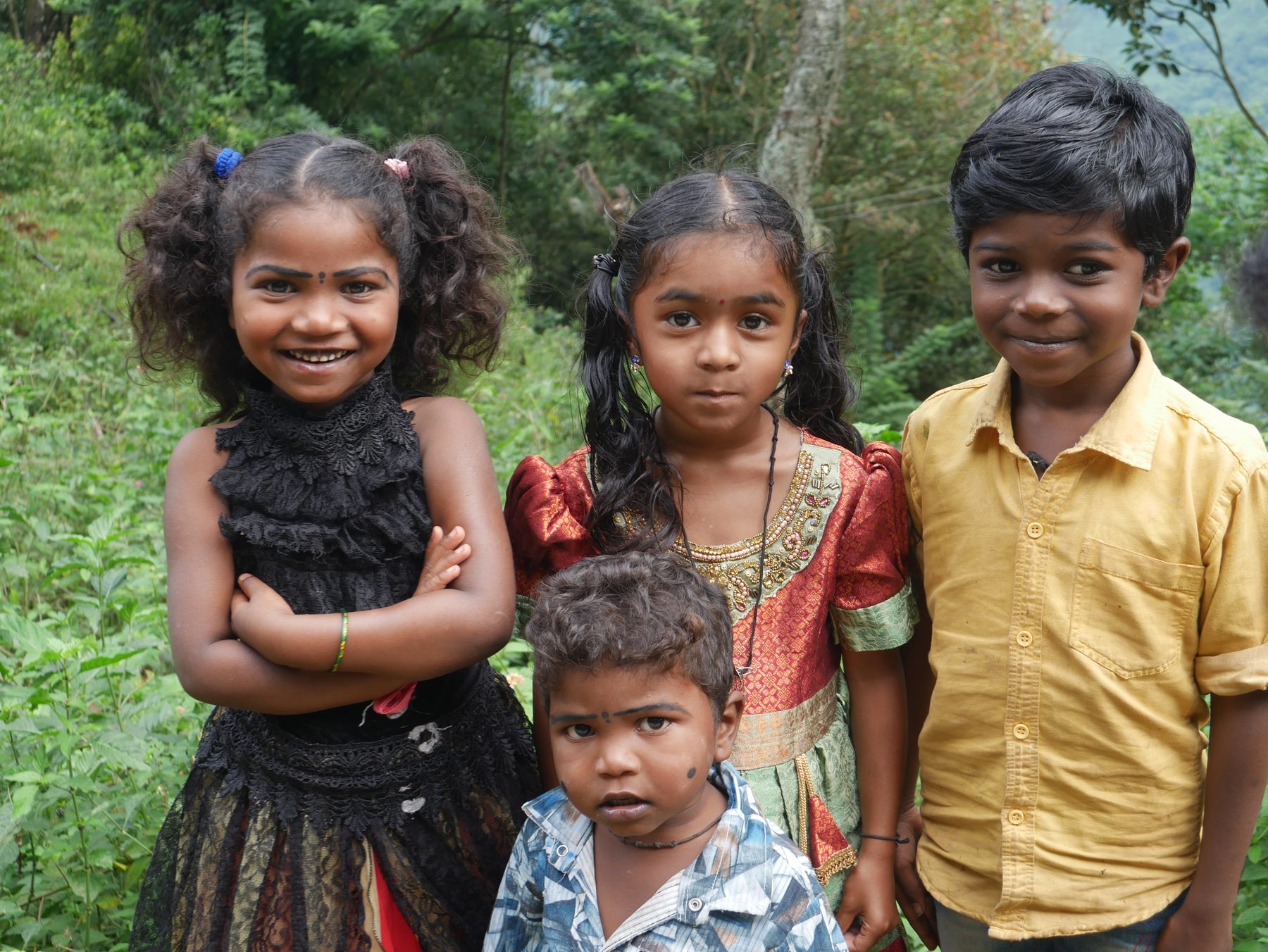 Four smiling children posing outdoors in front of a green hillside