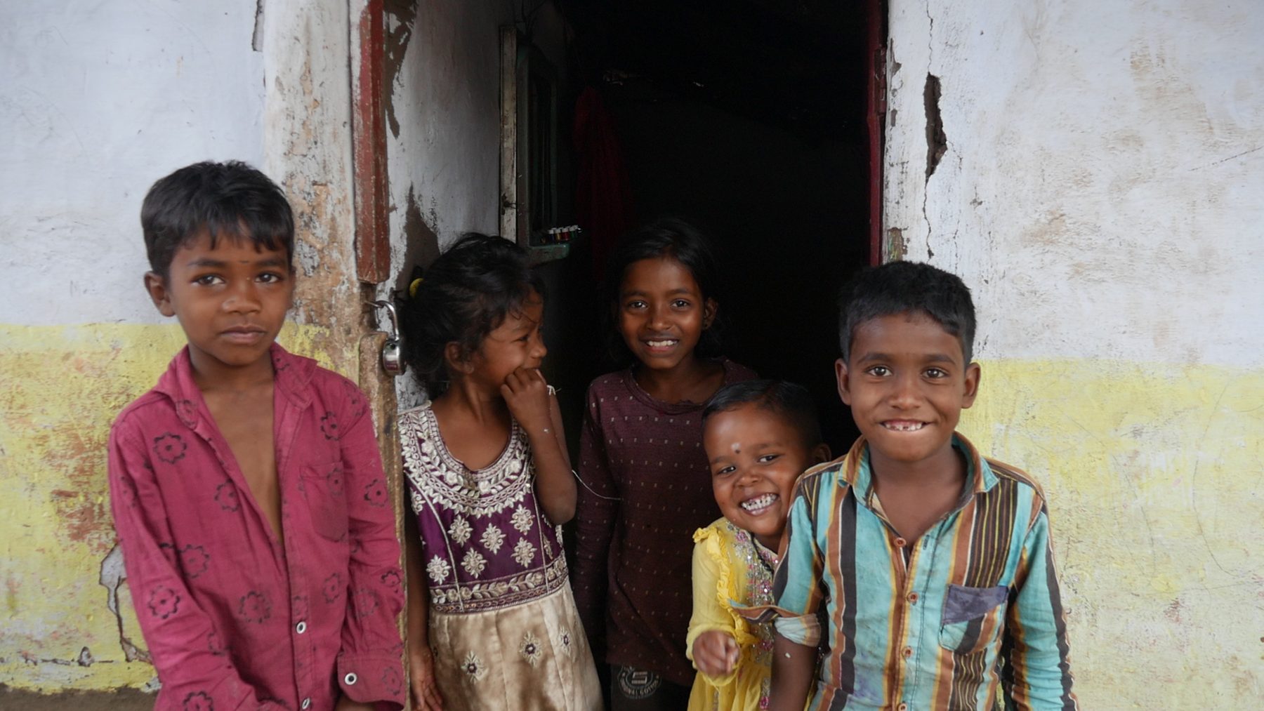 Five children smiling at the doorway of a whitewashed home